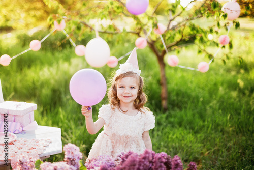 Happy birthday little girl making wish blowing candles on cake with pink decor in beautiful garden