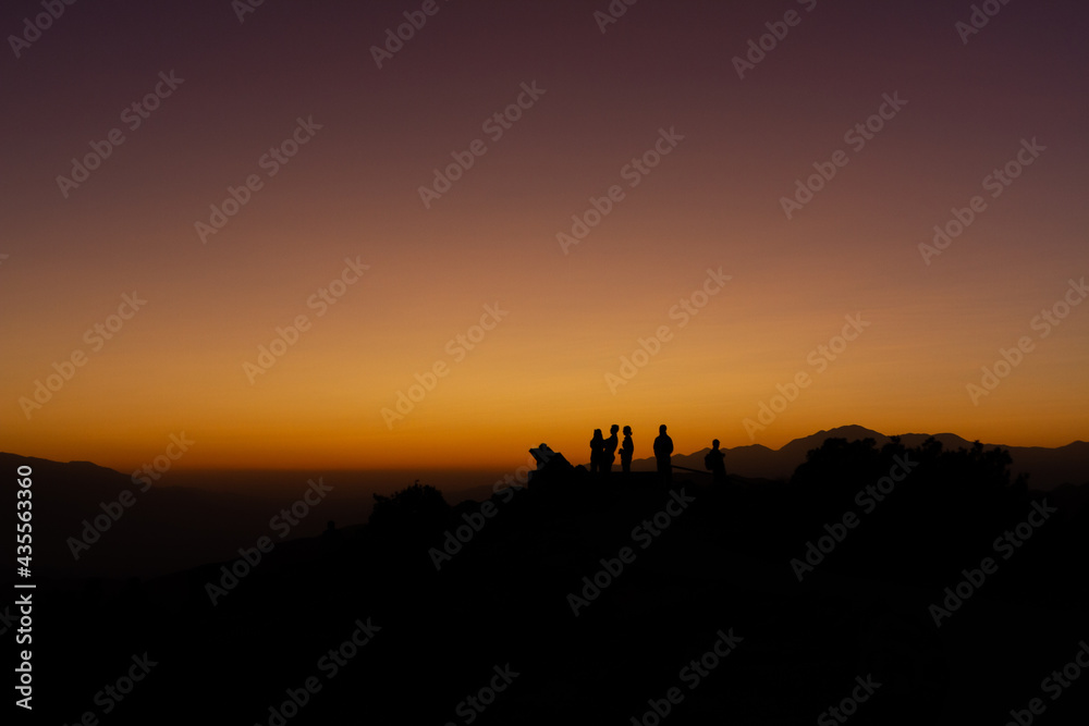 Medium shot of silhuette of people standing against orange colorful sunset sky in joshua tree national park in america