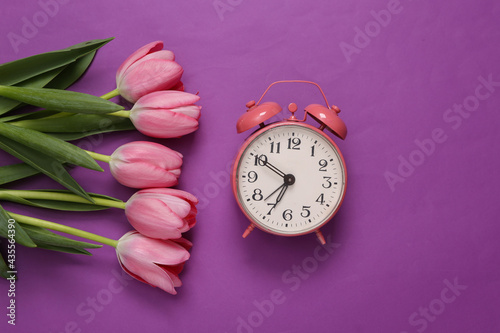 Pink tulips with alarm clock on purple background. Romantic concept