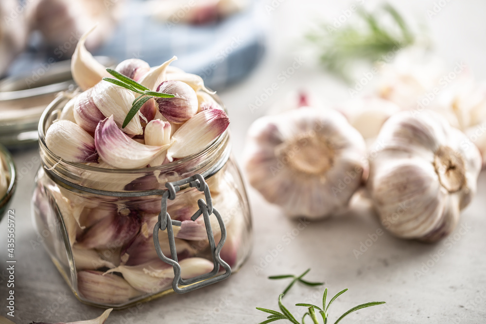Clear jar full of fresh aromatic garlic cloves with rosemary on the top as a decoration and aromatic garlic bulbs next to it Clear jar full of fresh aromatic garlic cloves with rosemary on the top as a decoration and aromatic garlic bulbs next to it
