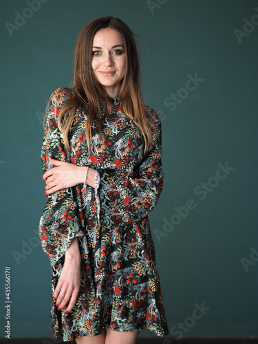 Brunette on a green background stands in a floral dress