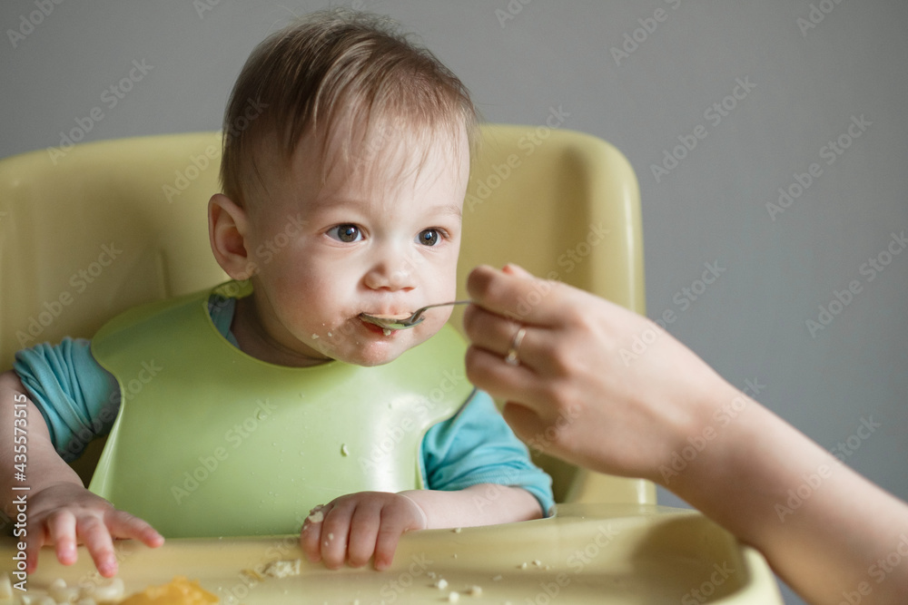 little child eats on gray background, mom feeds the baby with a spoon little child eats on gray background, mom feeds the baby with a spoon