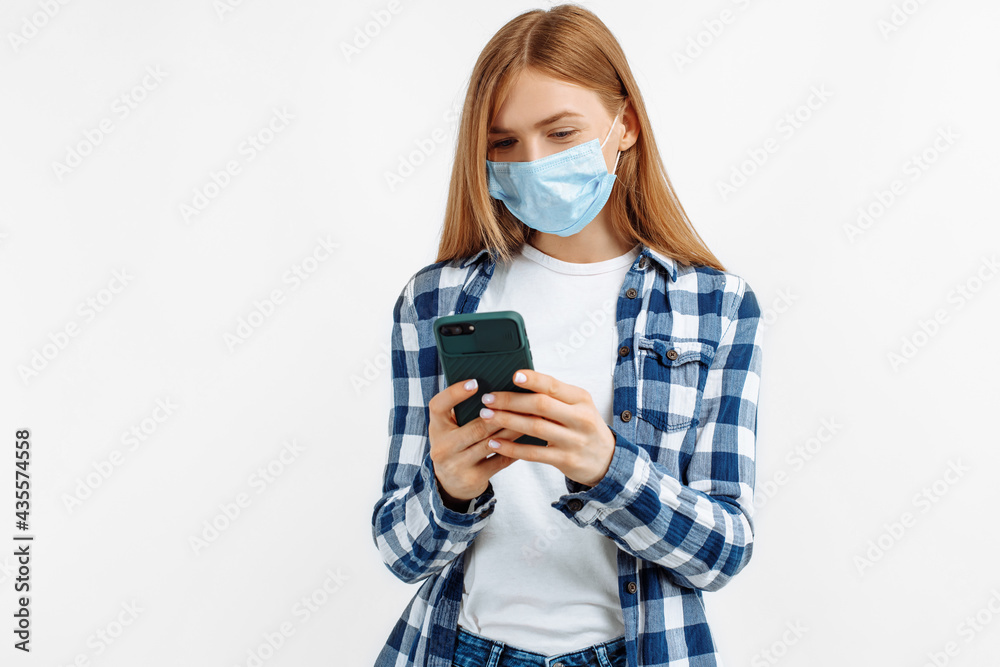 Portrait of a smiling young woman, wearing a medical mask for protection from covid 19, holding a smartphone on an white background Portrait of a smiling young woman, wearing a medical mask for protection from covid 19, holding a smartphone on an white background