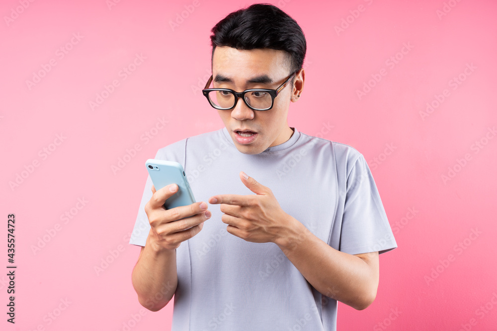 Portrait of Asian man using smartphone on pink background Portrait of Asian man using smartphone on pink background