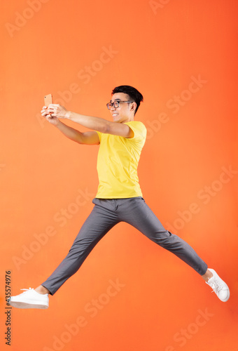 Asian man in yellow t-shirt jumping on orange background © Timeimage