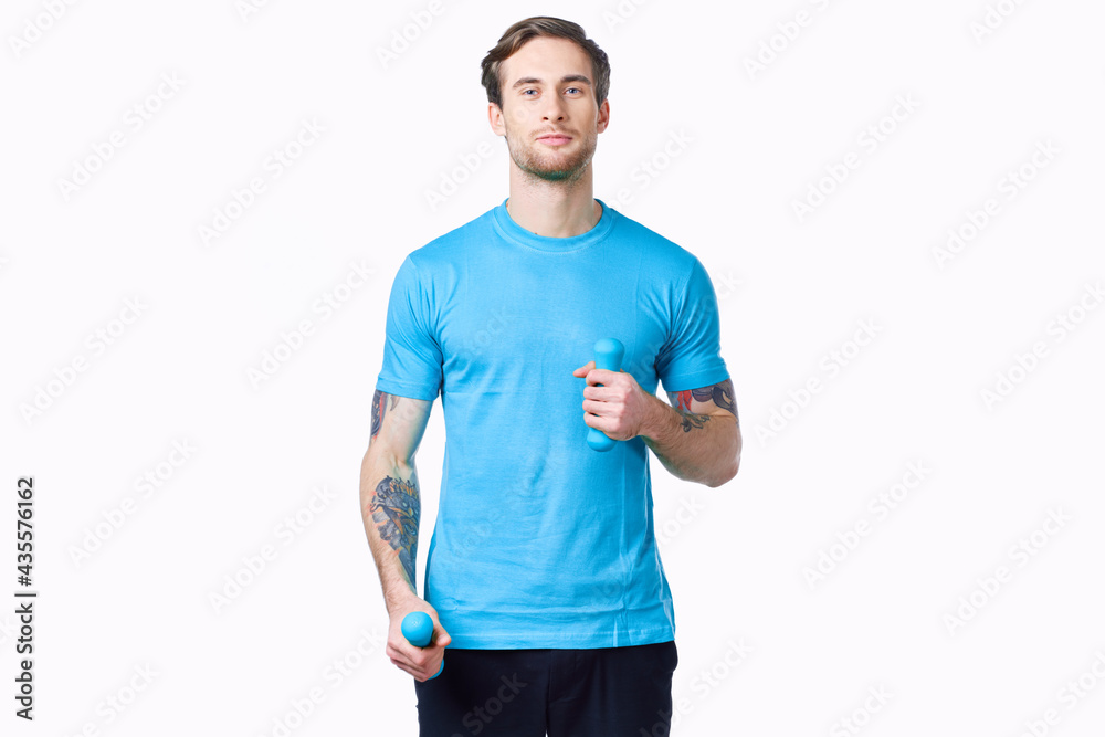 athlete with dumbbells on a light background and blue t-shirt pants tattoo athlete with dumbbells on a light background and blue t-shirt pants tattoo