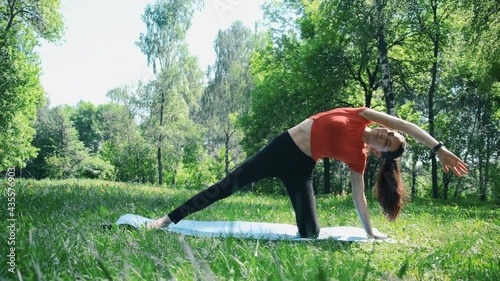 A woman in the forest does a back stretch while sitting on a mat in the park (forest). The camera is still there. General plan of stretching photo