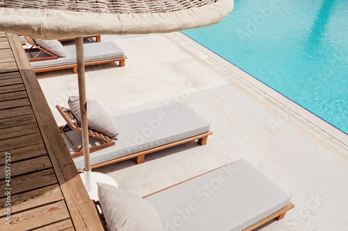 Photo Wooden sunbeds with ratang umbrellas near swimming pool