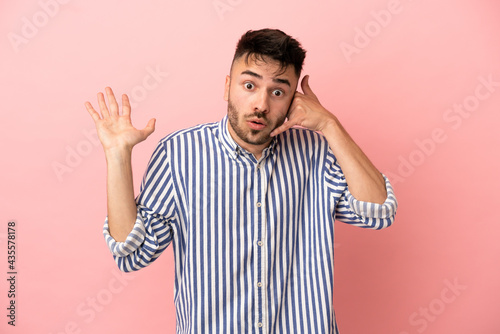 Young caucasian man isolated on pink background making phone gesture and doubting