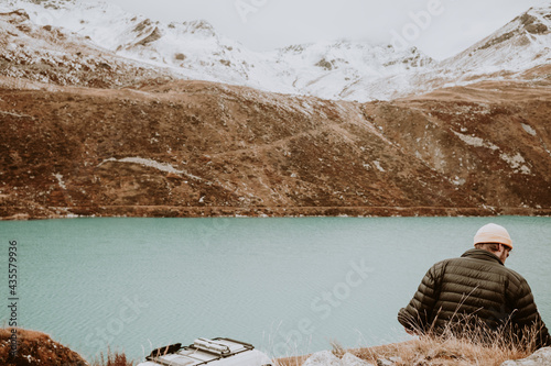 Mann in schwarzer Jacke und gelber Mütze sitzt in der Landschaft am Bergesee Lac de Moiry in der Schweiz mit Wohnmobil im Hintergrund photo