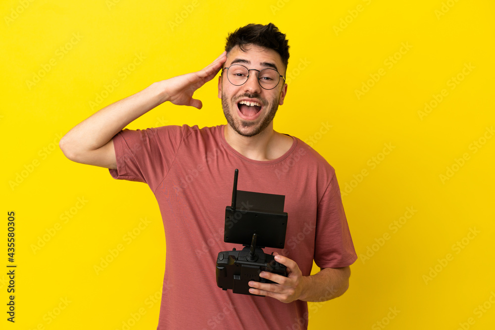 Man holding a drone remote control isolated on yellow background with surprise expression Man holding a drone remote control isolated on yellow background with surprise expression