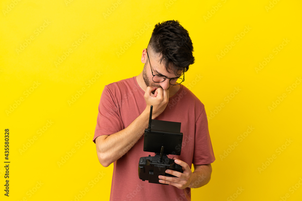 Man holding a drone remote control isolated on yellow background having doubts Man holding a drone remote control isolated on yellow background having doubts