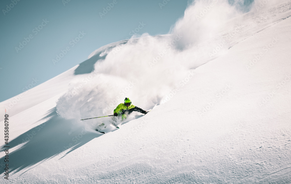 Skier rides in the mountain against the blue sky on fresh snow - obrazy, fototapety, plakaty 