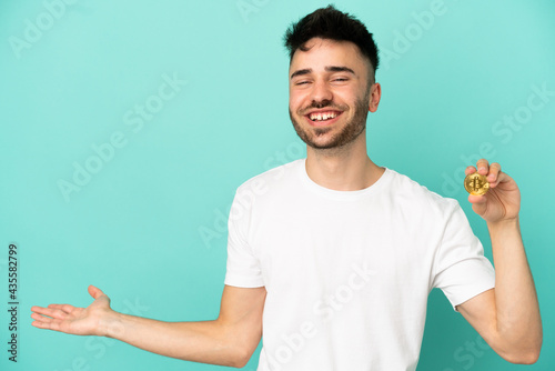 Young man holding a Bitcoin isolated on blue background extending hands to the side for inviting to come