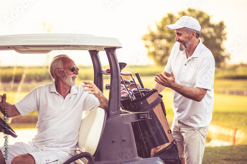 Two seniors golfer on golf court. Man sitting in golf car. photo