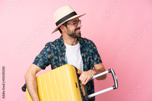 Young caucasian man over isolated background in vacation with travel suitcase and a hat photo