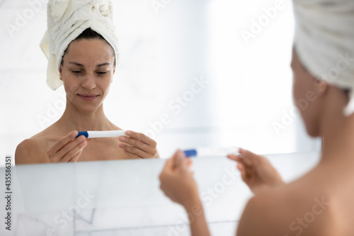 Smiling millennial girl looking at indefinite pregnancy test kit in bathroom  waiting result. Young woman learning about expecting baby  thinking over future motherhood  planning childbirth