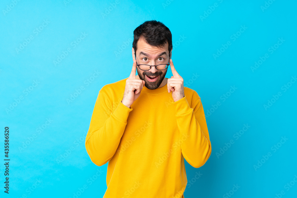 Young caucasian man over isolated blue background with glasses and surprised Young caucasian man over isolated blue background with glasses and surprised