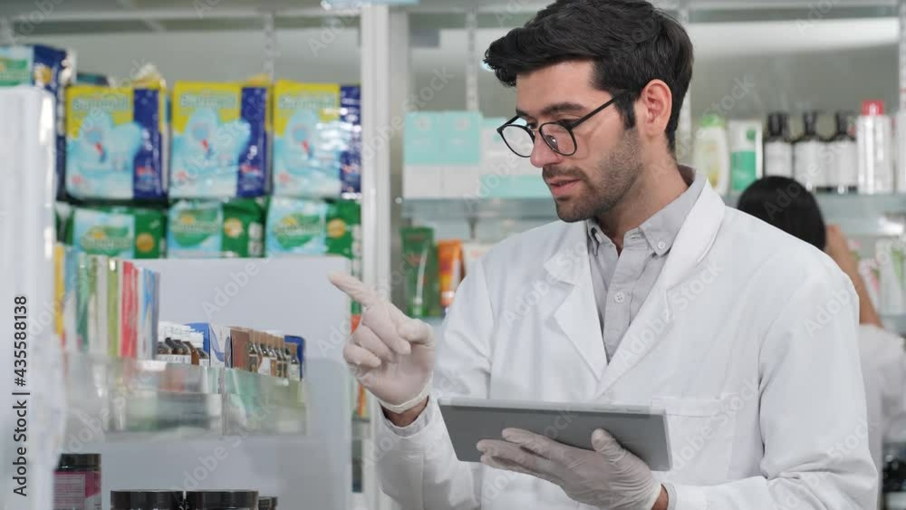 Male pharmacist using digital tablet and wear gloves reduce exposure checking stock inventory in modern pharmacy. Prevention of infectious diseases, touch, New Normal Concept Male pharmacist using digital tablet and wear gloves reduce exposure checking stock inventory in modern pharmacy. Prevention of infectious diseases, touch, New Normal Concept