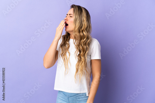 Young Brazilian woman isolated on purple background yawning and covering wide open mouth with hand