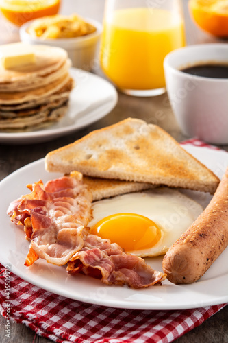 Traditional American breakfast with fried egg,toast,bacon and sausage on wooden table	