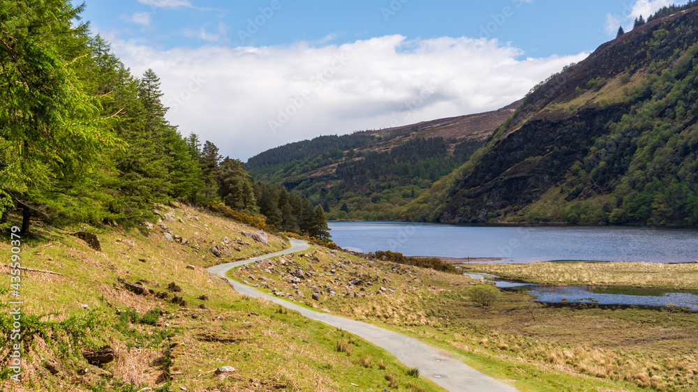 Hiking trail in a mountain lake landscape. Miners' road passing next to Glendalough Upper Lake in Wicklow mountains, Ireland. Hiking trail in a mountain lake landscape. Miners' road passing next to Glendalough Upper Lake in Wicklow mountains, Ireland.