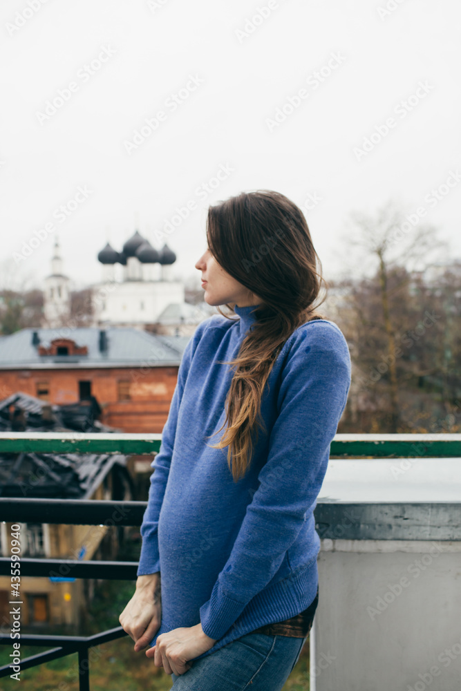 pregnant woman stands on the balcony against the background of the Orthodox church