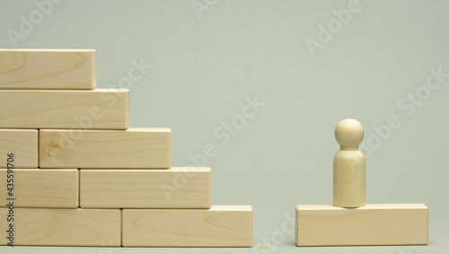 wooden figurine of a man stands on a staircase made of blocks on the first step
