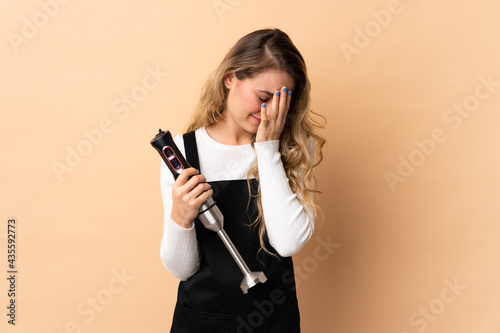Young brazilian woman using hand blender isolated on beige background with tired and sick expression