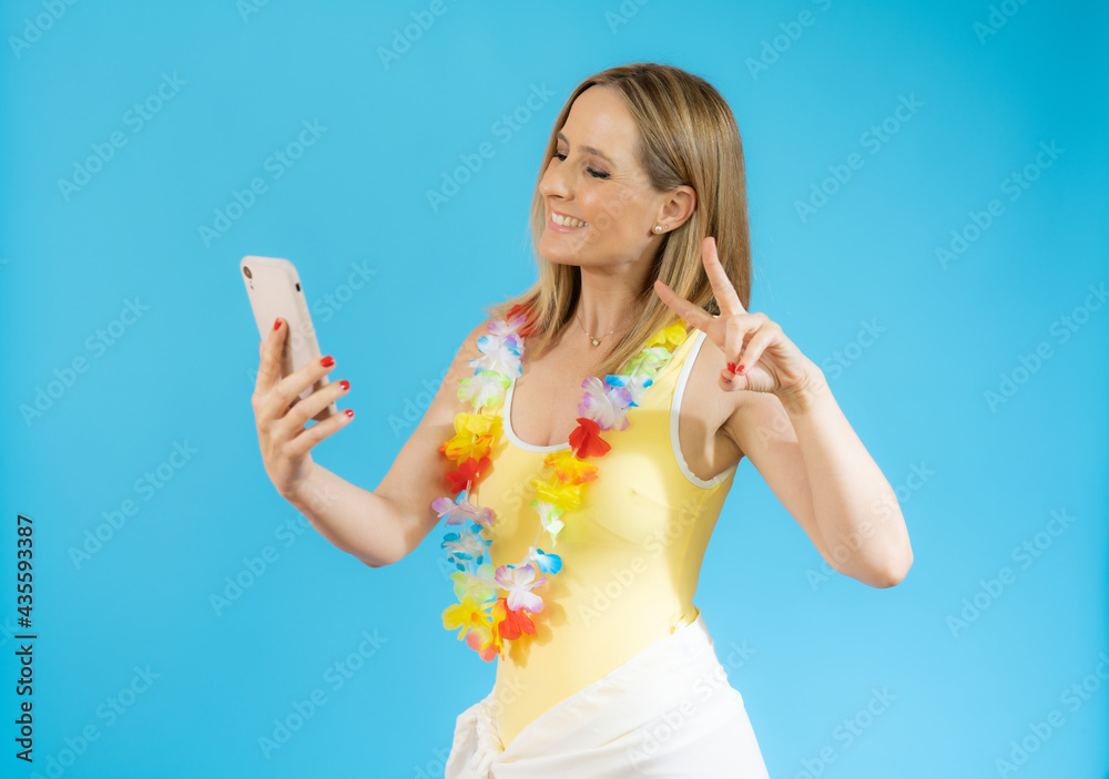 Portrait of a smiling casual woman in swimsuit holding smartphone over blue background Portrait of a smiling casual woman in swimsuit holding smartphone over blue background
