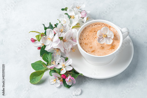 A cup of morning cappuccino and a branch of a flowering tree on a gray background.