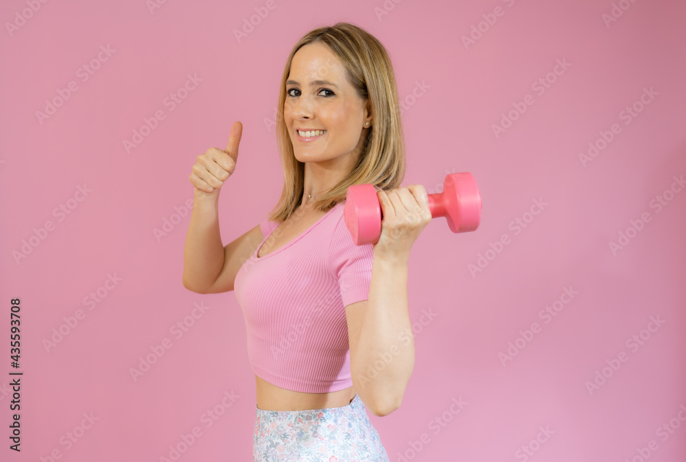 Cute athletic woman in sportswear with yoga mat with thumb up isolated on pink background