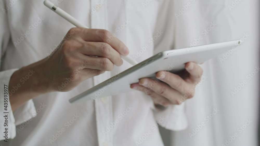 Close-up businessman signing a digital contract on a tablet using a stylus pen and checking work from a tablet while standing beside the window at the office. Close-up businessman signing a digital contract on a tablet using a stylus pen and checking work from a tablet while standing beside the window at the office.