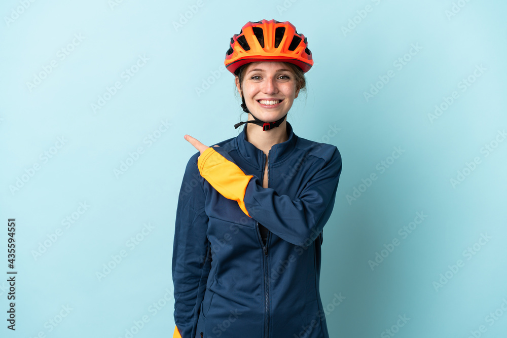 Young cyclist woman isolated on blue background pointing to the side to present a product - obrazy, fototapety, plakaty 