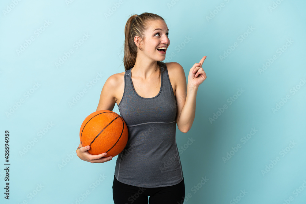 Young woman playing basketball isolated on blue background intending to realizes the solution while lifting a finger up Young woman playing basketball isolated on blue background intending to realizes the solution while lifting a finger up