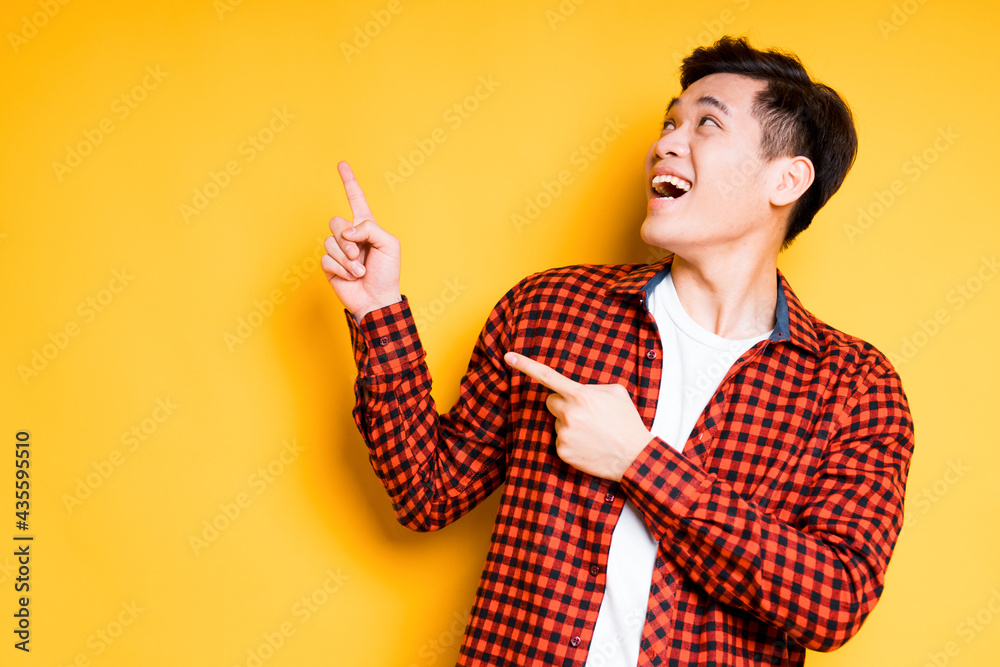 Cheerful asian guy in plaid shirt smiling and looking up showing hands to the side Cheerful asian guy in plaid shirt smiling and looking up showing hands to the side
