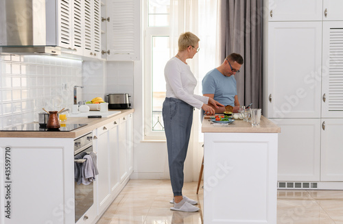 Portrait of lovely mature couple cooking together. Happy senior wife cooking breakfast for her husband in white kitchen