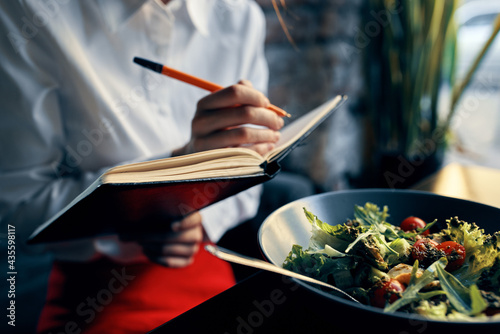 woman with notepad near the window and salad in a plate tomatoes fresh vegetables