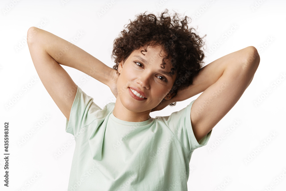 Young curly brunette woman smiling with hands clasped behind her neck Young curly brunette woman smiling with hands clasped behind her neck