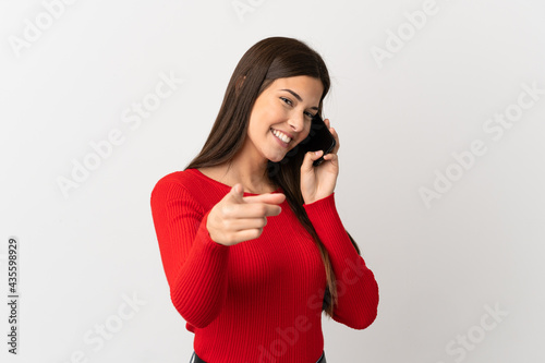 Teenager Brazilian girl using mobile phone over isolated white background pointing front with happy expression