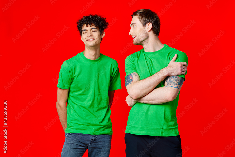 joyful friends in green t-shirts are standing next to red background joyful friends in green t-shirts are standing next to red background