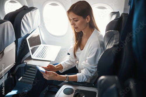 Calm young lady with two modern gadgets in the plane