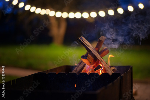 Wooden logs burning in the grill in the night garden decorated with lanterns. summer parties with grill cocept
