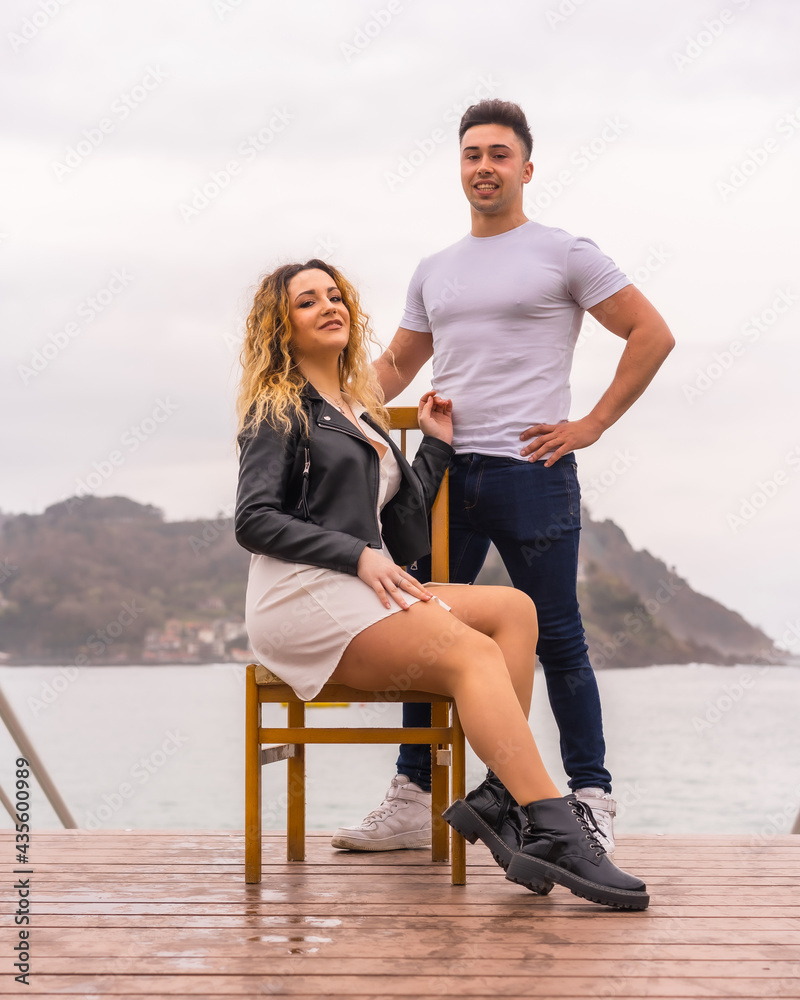 Fashionable pose of a Caucasian couple on vacation by the sea. Young woman sitting and boy next to her Fashionable pose of a Caucasian couple on vacation by the sea. Young woman sitting and boy next to her