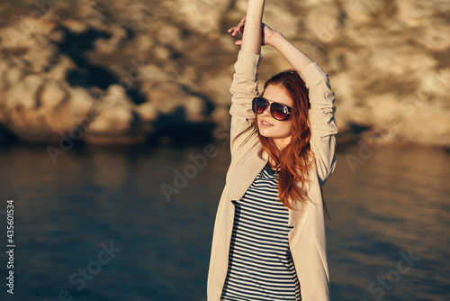 woman in a t-shirt holds her hands above her head near the sea in the mountains photo