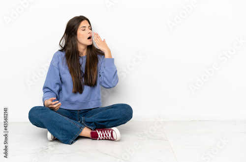 Photos Young woman sitting on the floor yawning and covering wide open mouth with hand