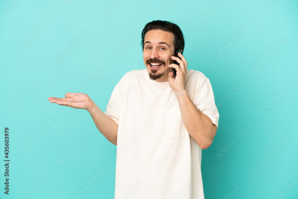 Young caucasian man isolated on blue background keeping a conversation with the mobile phone with someone Young caucasian man isolated on blue background keeping a conversation with the mobile phone with someone