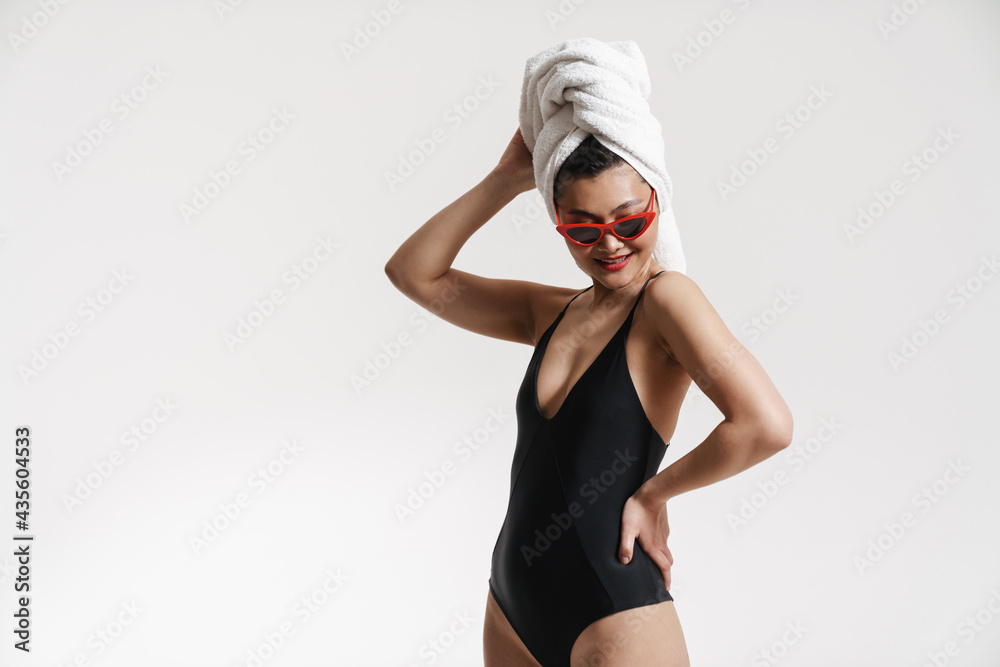 Fototapeta premium Brunette asian woman wearing swimsuit and towel smiling at camera