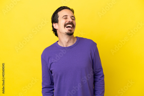 Young caucasian man isolated on yellow background laughing