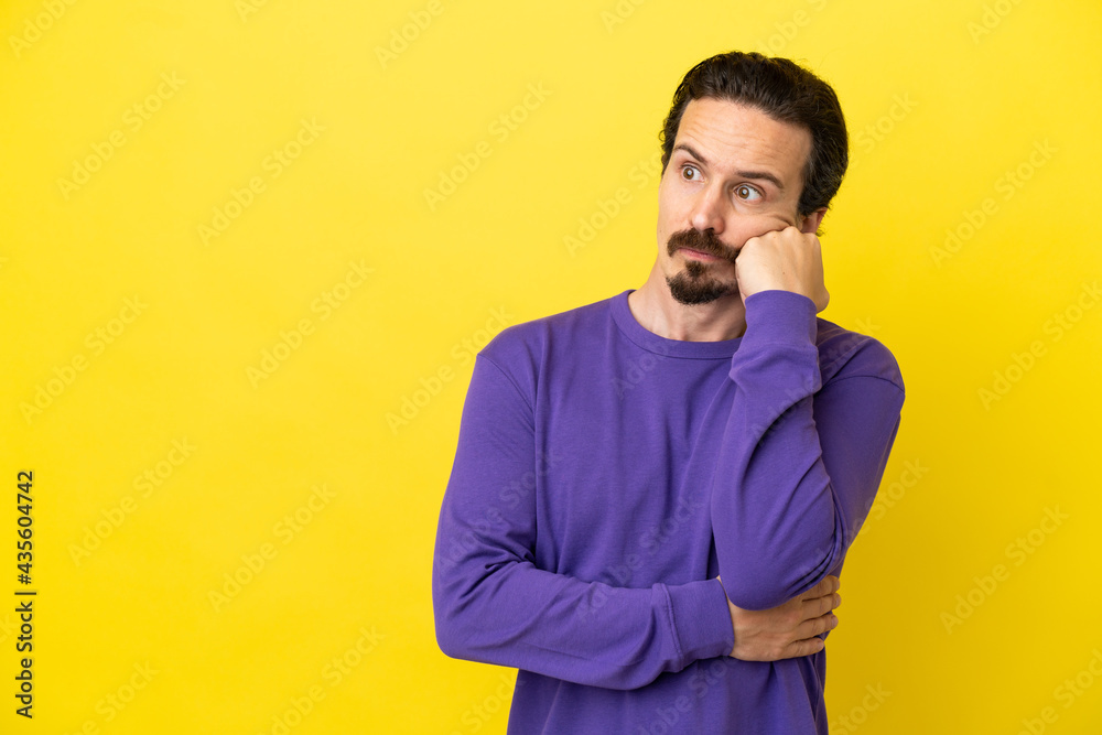 Young caucasian man isolated on yellow background with tired and bored expression